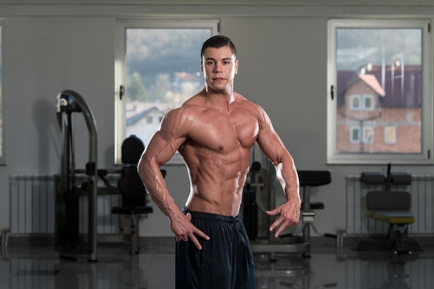 Retrato de un hombre en buena forma física que muestra su cuerpo bien entrenado en el gimnasio