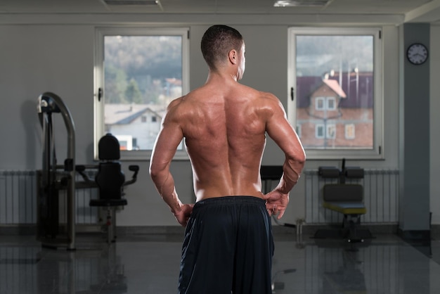 Retrato de un hombre en buena forma física que muestra su cuerpo bien entrenado en el gimnasio