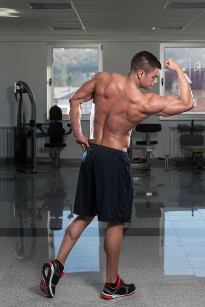 Retrato de un hombre en buena forma física que muestra su cuerpo bien entrenado en el gimnasio