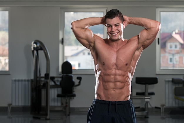 Retrato de un hombre en buena forma física que muestra su cuerpo bien entrenado en el gimnasio