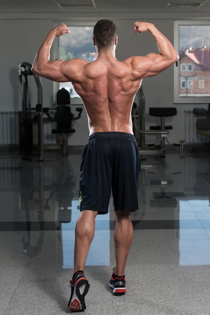 Foto retrato de un hombre en buena forma física que muestra su cuerpo bien entrenado en el gimnasio