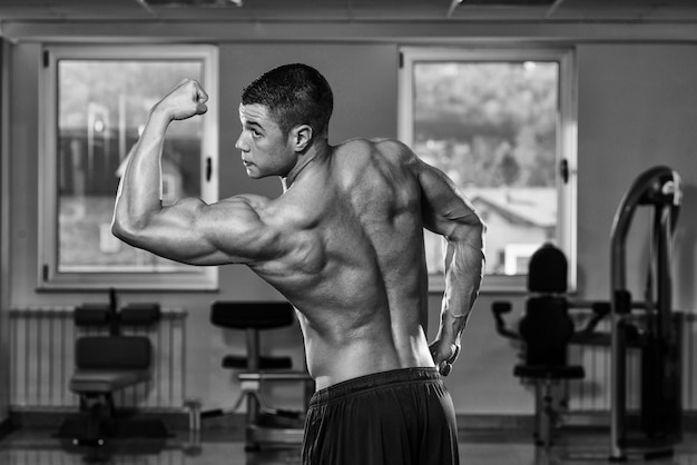 Retrato de un hombre en buena forma física que muestra su cuerpo bien entrenado en el gimnasio