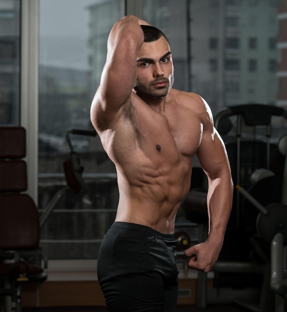 Retrato de un hombre en buena forma física que muestra su cuerpo bien entrenado en el gimnasio