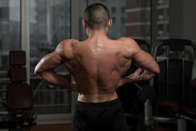 Retrato de un hombre en buena forma física que muestra su cuerpo bien entrenado en el gimnasio