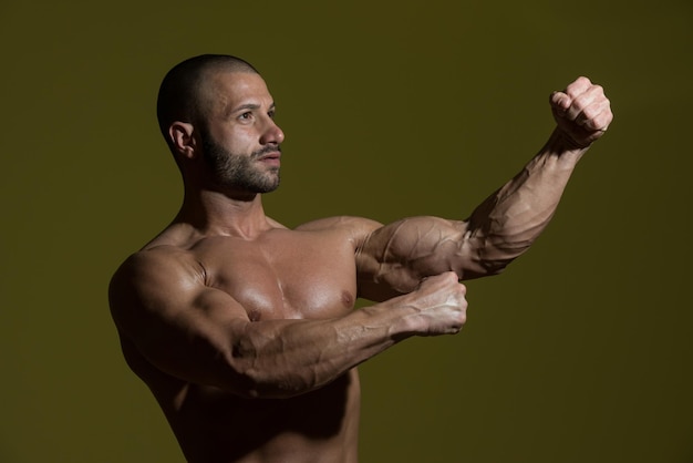 Retrato de un hombre en buena forma física que muestra su cuerpo bien entrenado en una habitación oscura