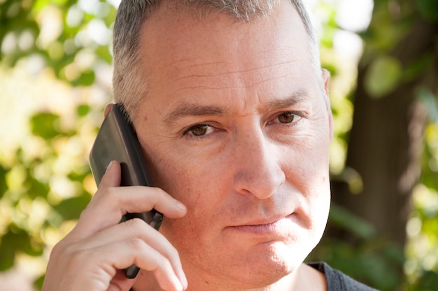 Retrato de hombre de cabello gris guapo seguro en el parque hablando por su teléfono móvil