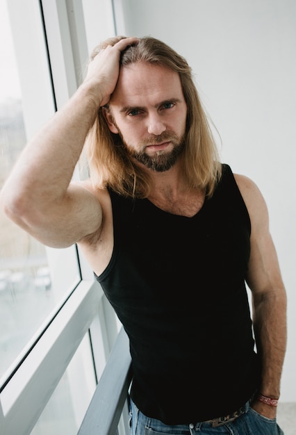 Retrato de hombre con cabello largo y rubio. Retrato del primer del muchacho joven que presenta en blanco. Toro brutal con ojos asombrosos toca el cabello