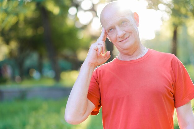 Retrato de un hombre calvo con una camiseta roja, expresión pensativa, sosteniendo un dedo cerca de su sien