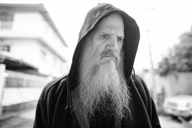 Retrato de hombre calvo maduro con larga barba gris en las calles al aire libre en blanco y negro