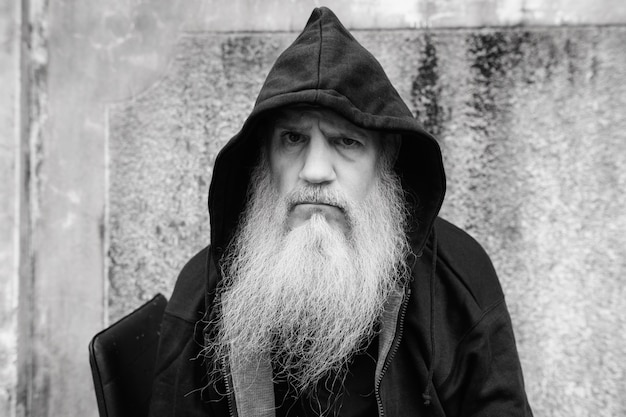 Retrato de hombre calvo maduro con larga barba gris contra el muro de hormigón de grunge al aire libre en blanco y negro