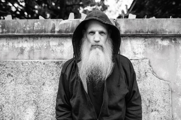 Retrato de hombre calvo maduro con larga barba gris contra el muro de hormigón de grunge al aire libre en blanco y negro