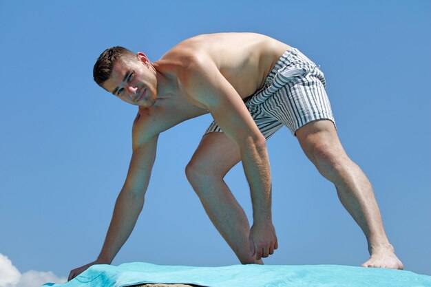 Retrato de un hombre sin camisa ajustando una toalla contra un cielo azul claro
