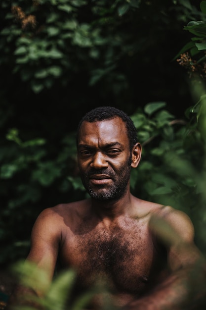 Retrato de un hombre sin camisa sentado contra las plantas