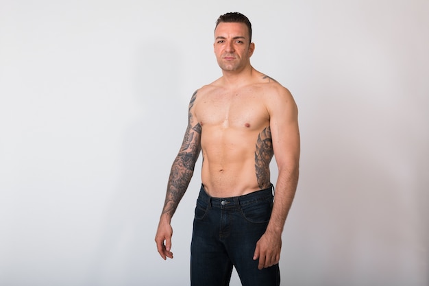 Retrato de hombre sin camisa con tatuajes contra la pared blanca