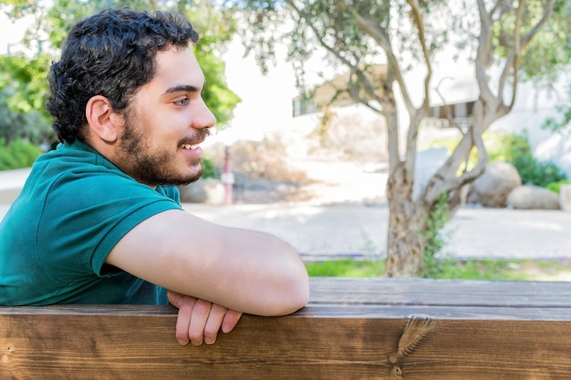 Retrato de un hombre cansado casual descansando sentado en un banco en el parque de la ciudad