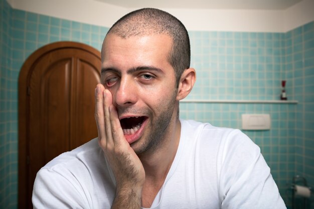 Retrato de un hombre cansado mirando en el espejo en su baño