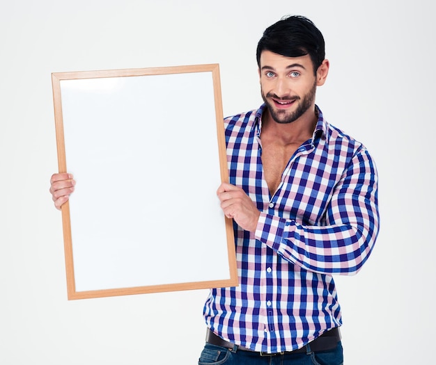 Retrato de un hombre casual sonriente sosteniendo tablero en blanco aislado en una pared blanca