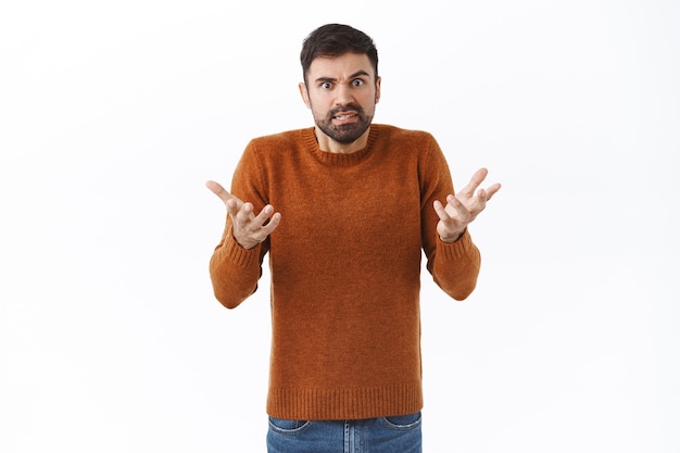 Retrato de hombre caucásico barbudo enfermo y cansado, frustrado discutiendo, peleando, levantando las manos consternado, encogiéndose de hombros confundido con cara molesta y molesta, pared blanca