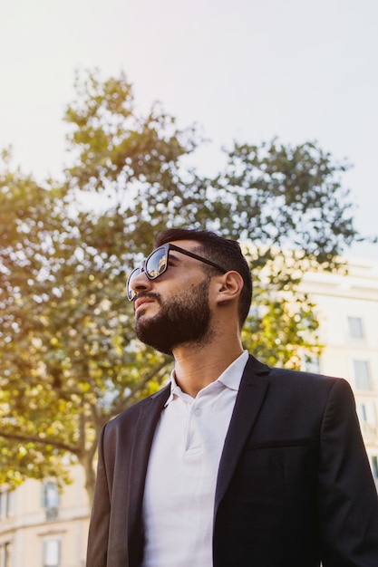 Retrato de hombre caucásico guapo con barba y gafas de sol, en una calle de la ciudad. Imagen vertical