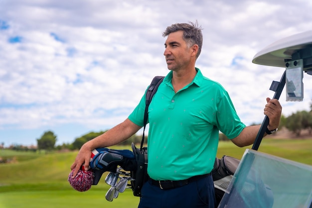 Retrato de un hombre caucásico jugando al golf junto al buggy en un día nublado