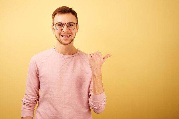 Retrato de un hombre caucásico que usa anteojos con una cara sonriente y alegre apuntando hacia un lado aislado en un fondo amarillo con ropa informal le recomienda usar espacio para copiar