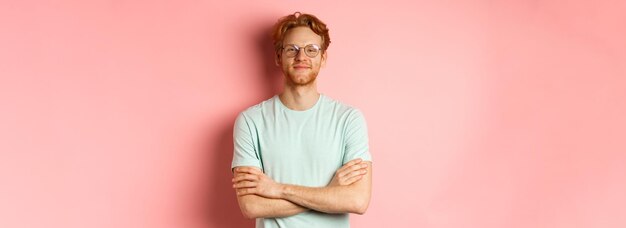 Retrato de un hombre caucásico satisfecho con el pelo rojo y la barba cruza los brazos en el pecho y sonríe con smu