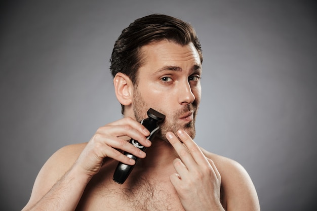 Foto retrato de un hombre concentrado sin camisa que afeita la barba