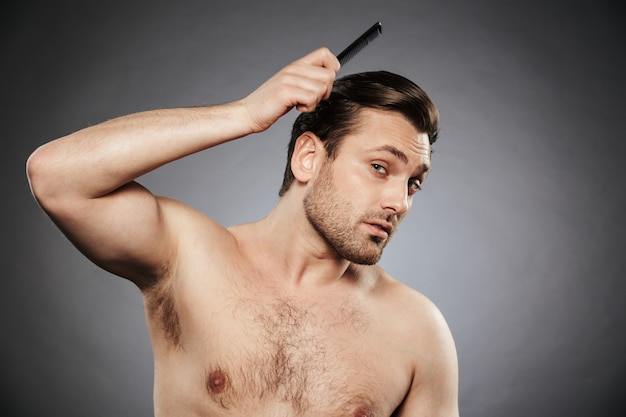 Foto retrato de un hombre concentrado sin camisa que se peina