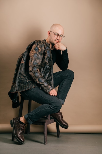 Retrato del hombre confiado calvo adulto en la ropa elegante que presenta sobre fondo del papel de café en estudio.