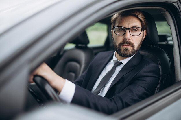 Retrato de hombre confiado en gafas y traje conduciendo coche