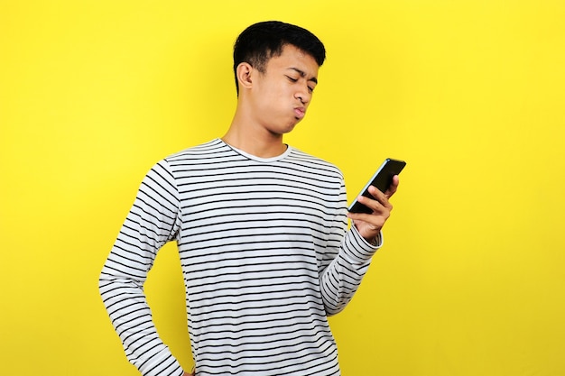 Retrato de hombre confundido mirando smartphone, aislado sobre fondo amarillo