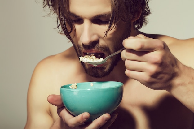 Retrato de hombre con cuchara de cerca. Cereales para el desayuno, comida sana para hombre o deportista sobre fondo gris.