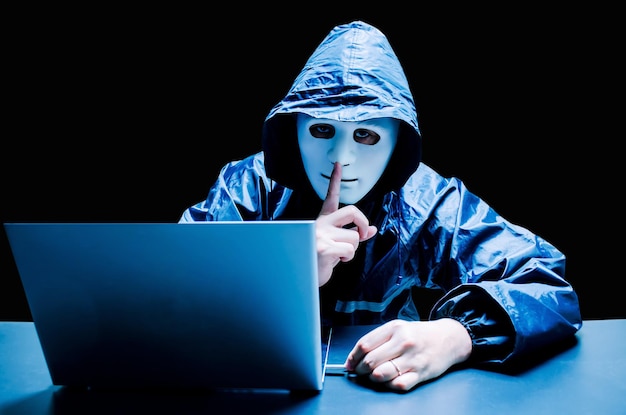 Retrato de un hombre con el dedo en los labios usando una computadora portátil en la mesa contra un fondo negro