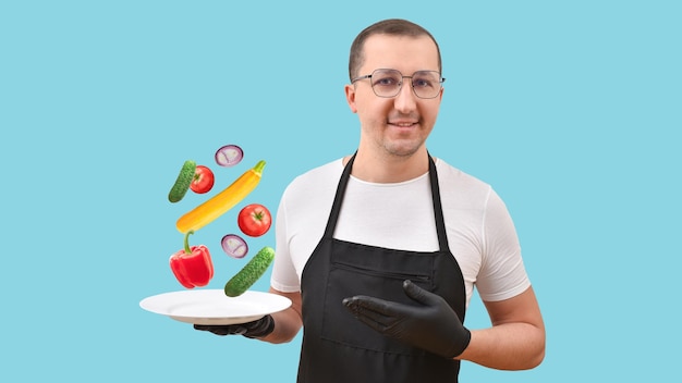 Retrato de un hombre con un delantal negro con un plato de comida fresca en las manos sobre un fondo azul.