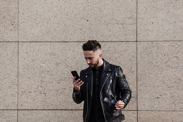 Retrato de un hombre desconcertado mirando el teléfono móvil sobre el fondo de la pared urbana. copia espacio