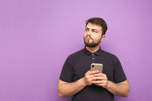 Retrato de un hombre desconcertado en la ropa casual se encuentra con un teléfono inteligente en sus manos