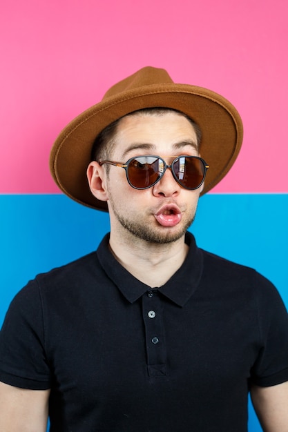 retrato de un hombre elegante en polo negro, gafas de sol y un sombrero marrón. Chico elegante