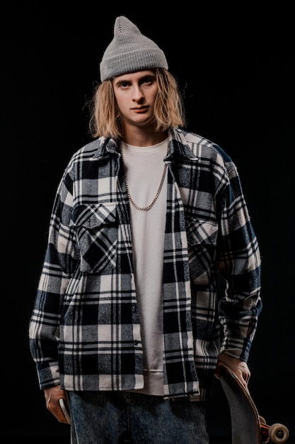 Retrato de un hombre elegante sosteniendo una patineta en el estudio. Primer plano de un skater sonriente posando sobre un fondo negro.