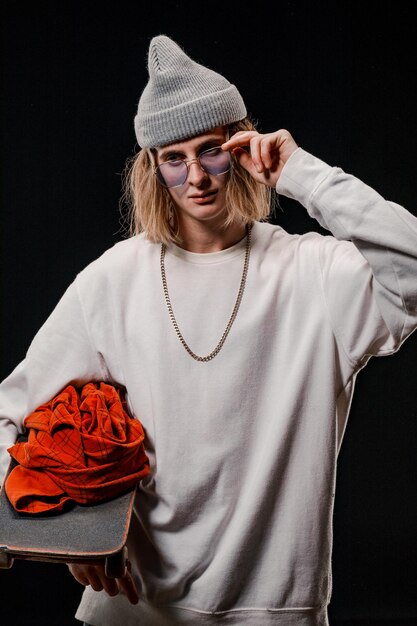 Retrato de un hombre elegante sosteniendo una patineta en el estudio. Primer plano de un skater sonriente posando sobre un fondo negro.