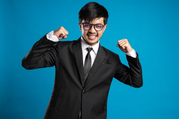 Retrato de hombre emocionado con la boca abierta vestido con ropa formal dando puño contra el fondo azul.