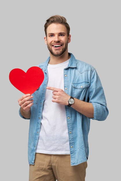 Retrato de hombre encantador mantenga la mano de papel en forma de corazón de la tarjeta use camisa de estilo casual aislado sobre gris