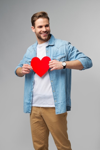 Foto retrato de hombre encantador mantenga la mano de papel en forma de corazón de la tarjeta use camisa de estilo casual aislado sobre la pared gris