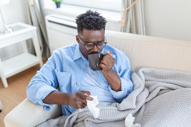 Retrato de un hombre enfermo con alergia a la gripe, gérmenes, tos fría, hombre enfermo con té sentado debajo de la manta con fiebre alta y gripe descansando y bebiendo bebidas calientes