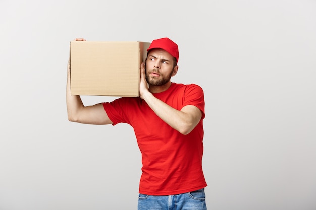 El retrato del hombre de entrega hermoso caucásico curioso escucha dentro de un paquete de la caja.