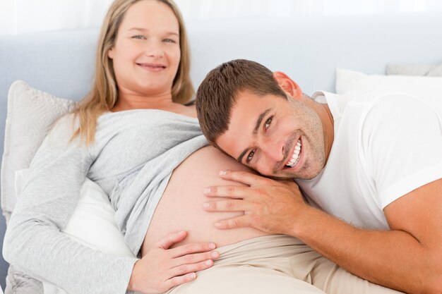 Retrato de un hombre escuchando el vientre de su esposa embarazada