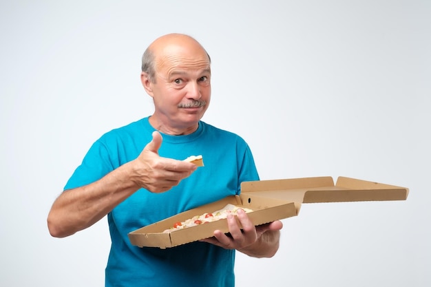 Retrato de un hombre europeo maduro comiendo una rebanada de pizza En sus manos sostiene una caja de comida Sesión de estudio