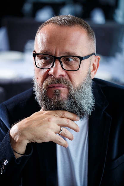 Retrato de un hombre de éxito adulto canoso con barba empresario con gafas con un rostro serio en una chaqueta