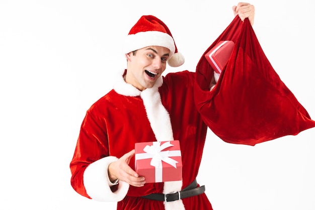 Retrato de hombre feliz de 30 años en traje de santa claus y sombrero rojo con bolsa festiva con cajas de regalo