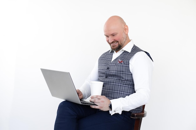 Retrato de hombre feliz en chaleco gris blue jeans camisa blanca sosteniendo portátil taza de café para llevar mirada