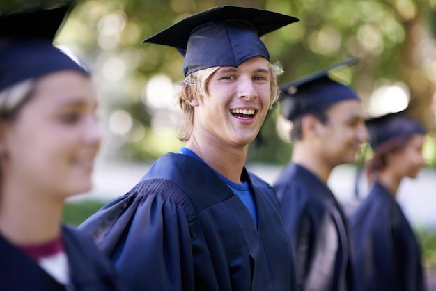 Retrato de hombre feliz y estudiantes en graduación al aire libre para educación, aprendizaje o calificación Persona masculina o graduada sonríe con el grupo para obtener un certificado superior, diploma o título en la ceremonia del campus